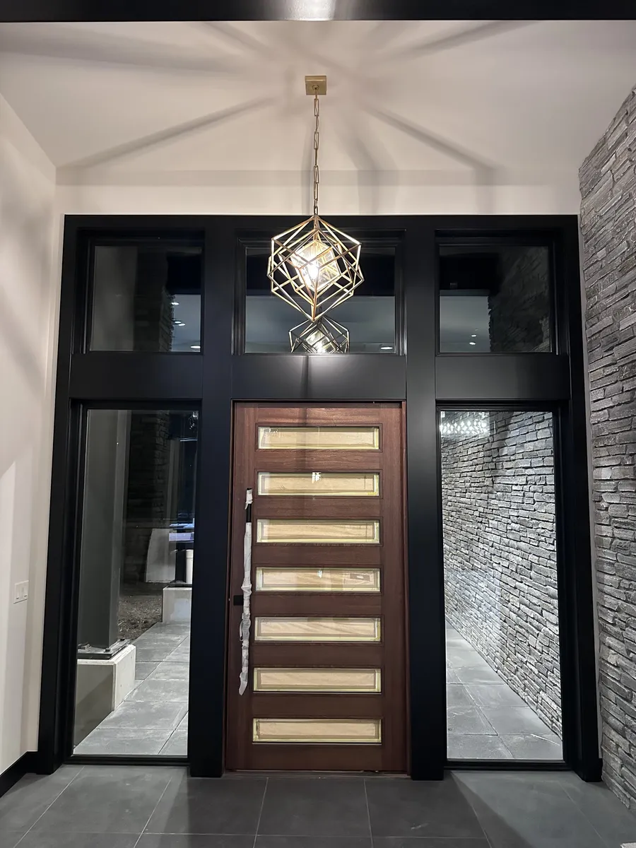 Wood front door framed by wide black casing, transom windows and a brass pendant