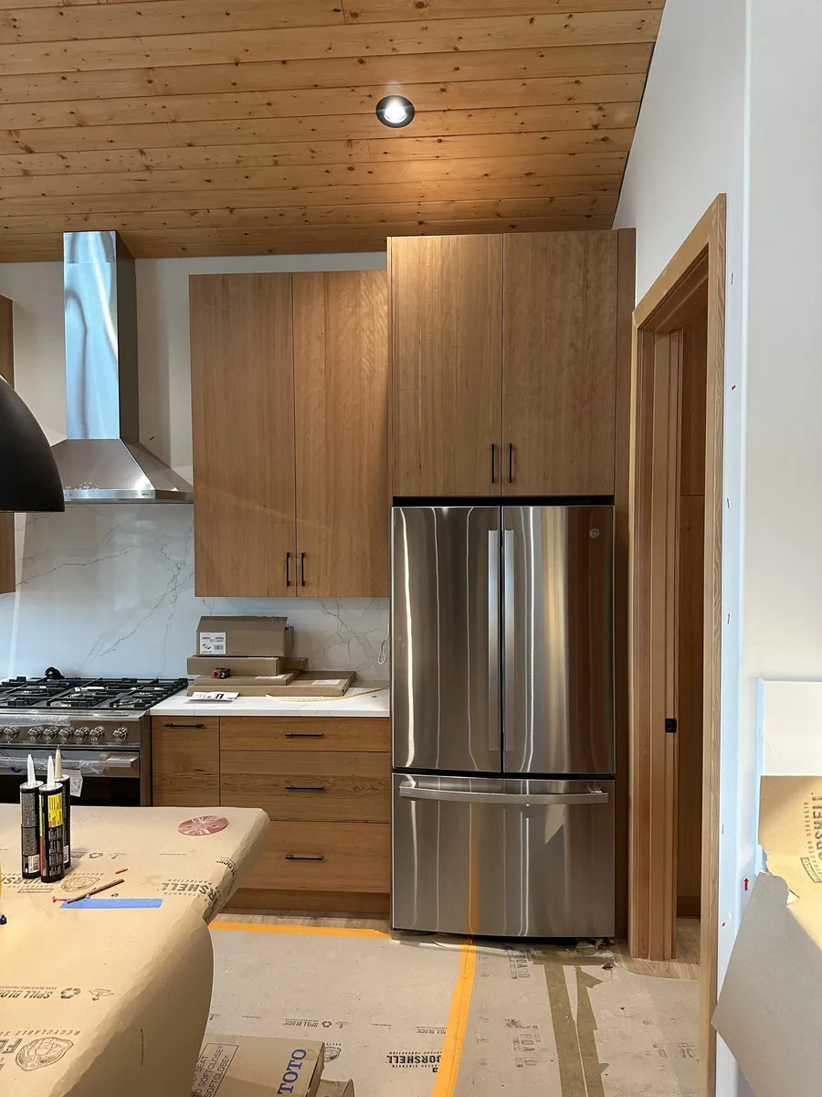 Refrigerator surround with tall wood upper cabinet and door casing